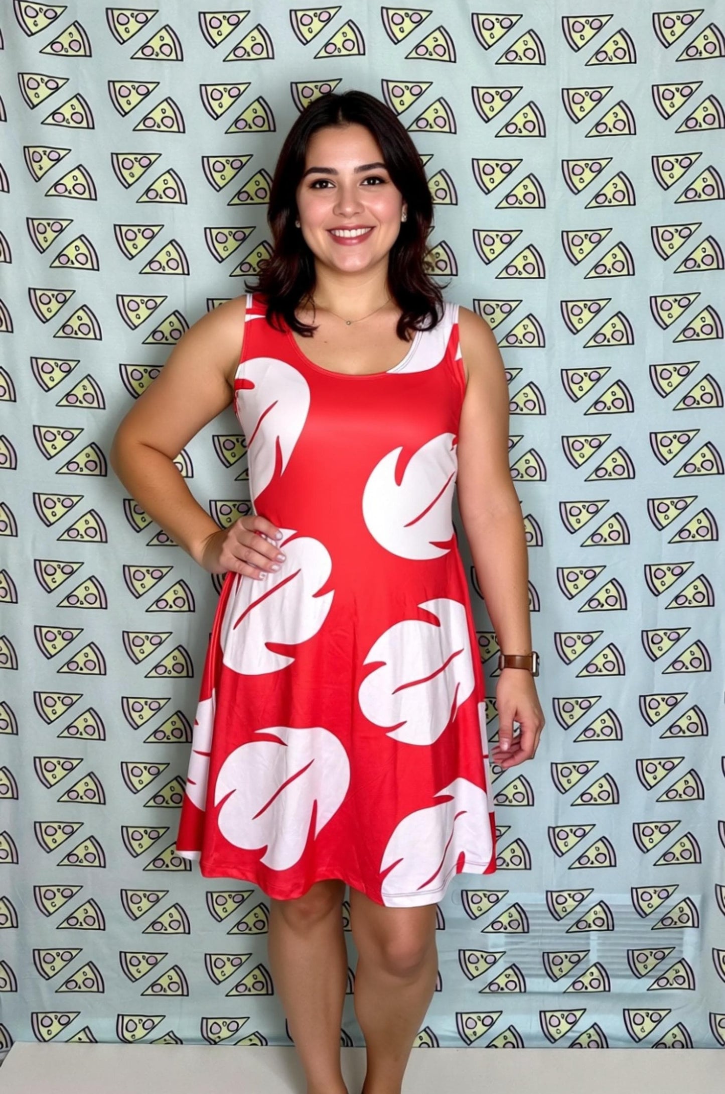 A woman wearing a red dress with white leaf patterns stands in front of a patterned background.