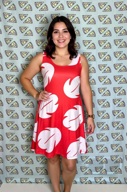 A woman wearing a red dress with white leaf patterns stands in front of a patterned background.