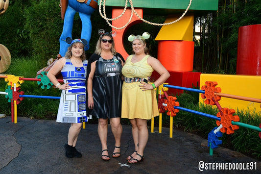 May include: Three sleeveless dresses featuring Star Wars character designs. The left dress is white and blue with R2-D2 graphics. The center dress is black with Darth Vader chest plate details. The right dress is yellow with C-3PO chest plate graphics.
